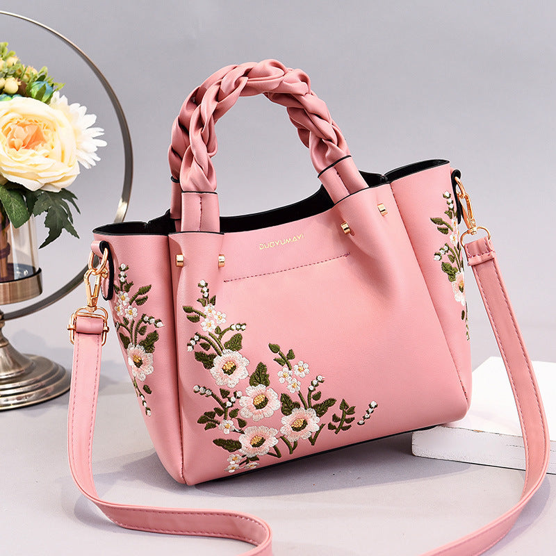 Pink handbag with floral embroidery on a light gray background