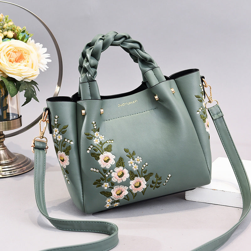 Green handbag with floral embroidery on a light gray background