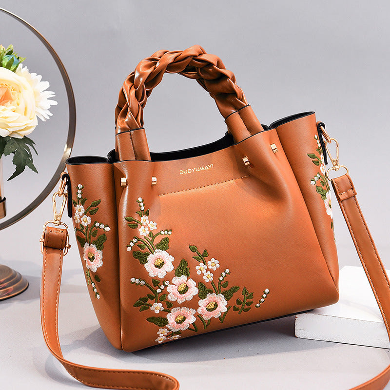 Brown handbag with floral embroidery on a light gray background