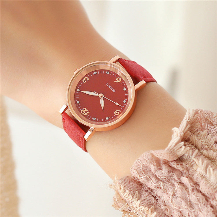 Wristwatch with red strap and rose gold case on a wrist, blurred background