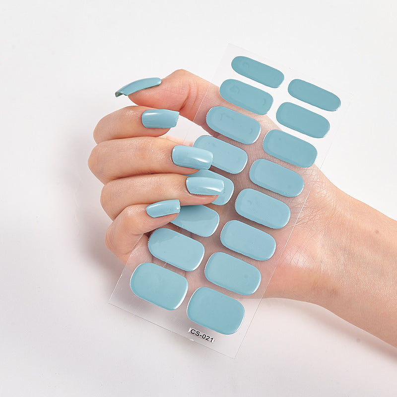 Hand holding a sheet of light blue nail stickers against a white background