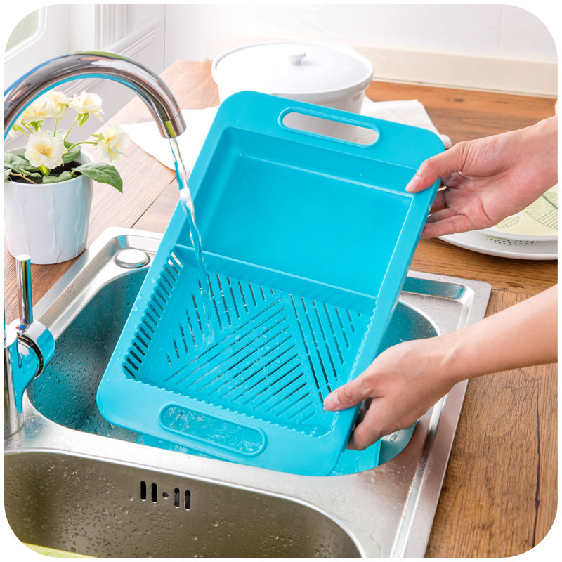 Person washing a blue cutting board and strainer in a kitchen sink.
