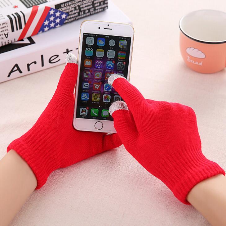 Person wearing red gloves using a smartphone on a table with books and a mug in the background.