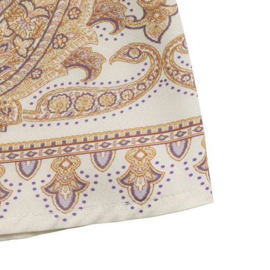 Close-up of a fabric with intricate paisley pattern in gold and purple on a white background