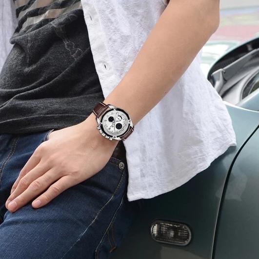 White-dial MEGIR quartz watch with brown strap worn on a wrist beside jeans