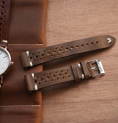 Close-up of brown perforated leather watch strap with metal buckle and stitched edges