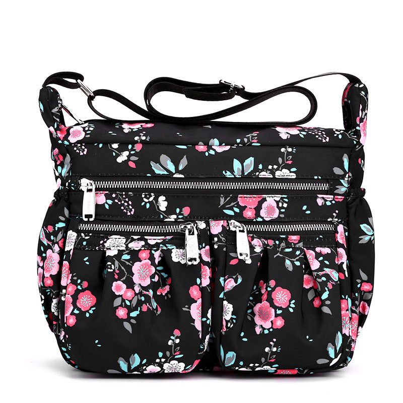 Large-capacity crossbody bag in black with pink floral print and front zip pockets.