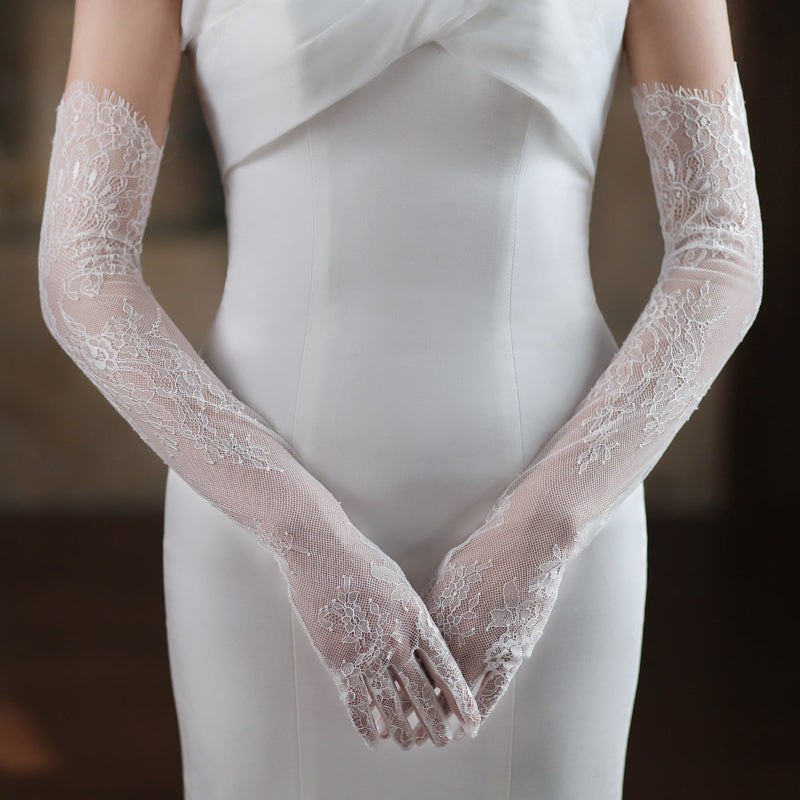 Lace gloves worn with a white dress against a dark background