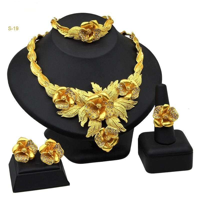 Gold jewelry set including necklace, earrings, and bracelet on a black stand.