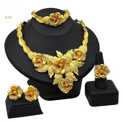 Gold jewelry set including necklace, earrings, and bracelet on a black stand.