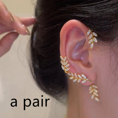 Gold leaf-shaped earring being worn on an ear with a neutral background