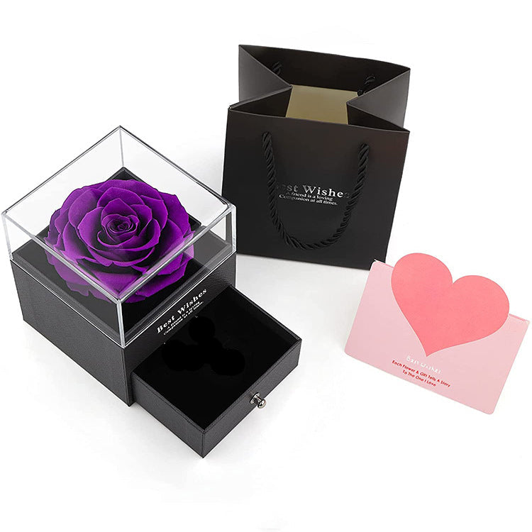 Purple rose in a clear box with a black gift bag and pink card on a white background
