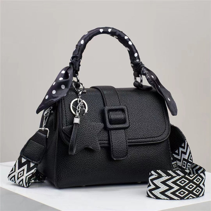 Black handbag with a decorative strap on a light gray background