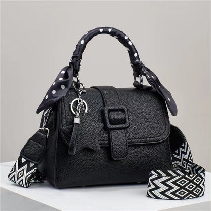 Black handbag with a decorative strap on a light gray background