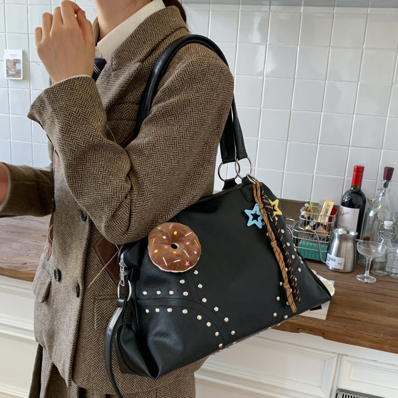 Person wearing a brown coat holding a black handbag with decorative elements in a kitchen setting.