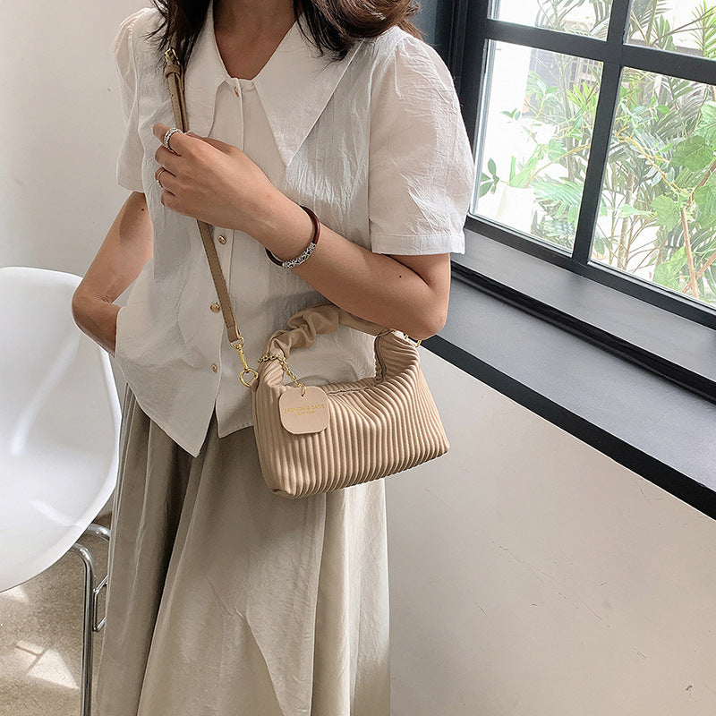 Person holding a beige handbag indoors near a window