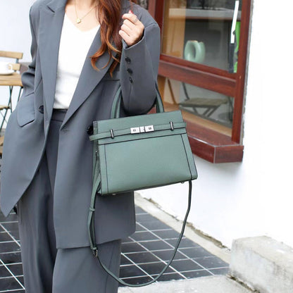 Person wearing a gray suit holding a green handbag outdoors.