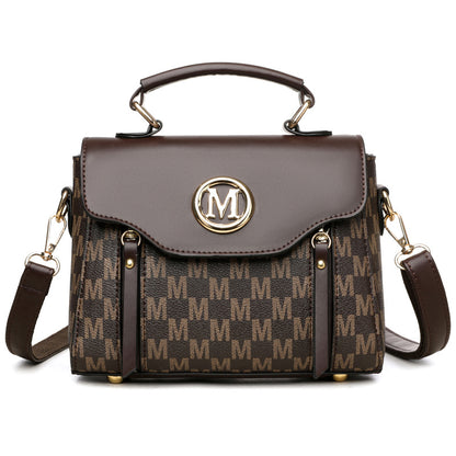 Brown handbag with gold accents and a prominent 'M' logo on a white background