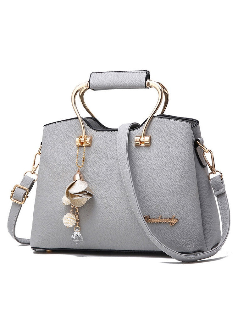 Gray handbag with gold accents and a decorative charm on a white background