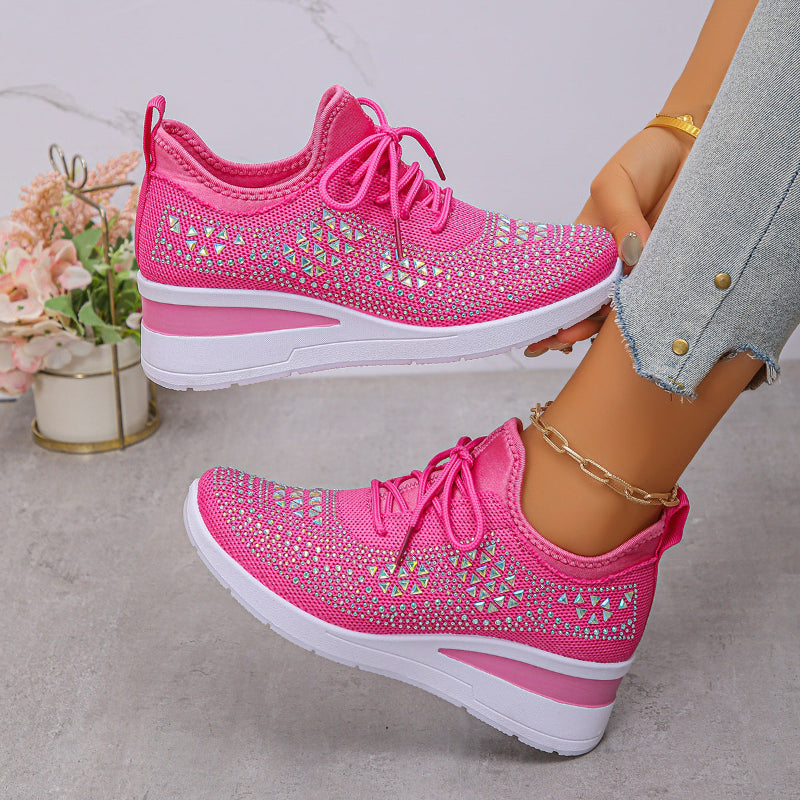 Pink sneakers with rhinestone details worn by a person on a light gray background
