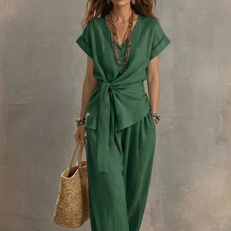Woman wearing a green jumpsuit holding a straw bag against a gray background