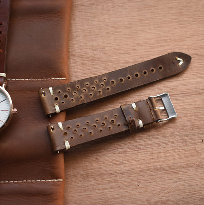 Brown perforated leather watch strap with metal buckle, rounded tip and keeper loop