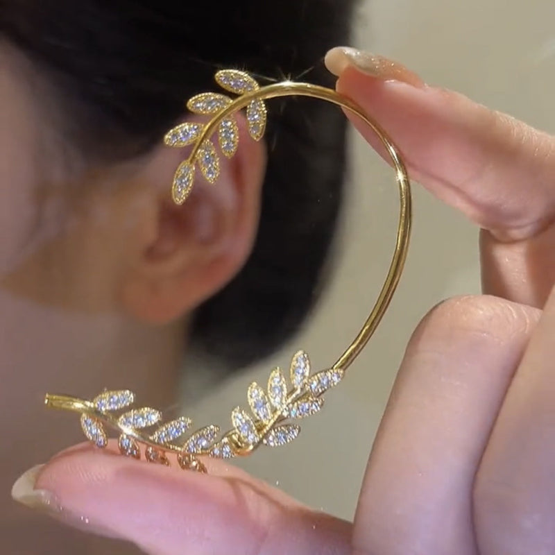 Gold leaf-shaped earring being held near an ear