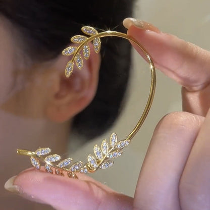 Gold leaf-shaped earring being held near an ear