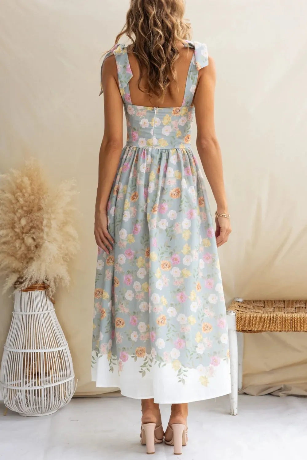 Woman wearing a floral dress standing in a minimalistic room with a neutral background.