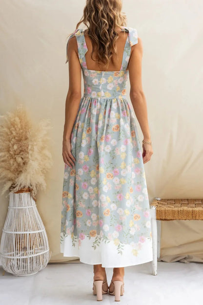 Woman wearing a floral dress standing in a minimalistic room with a neutral background.