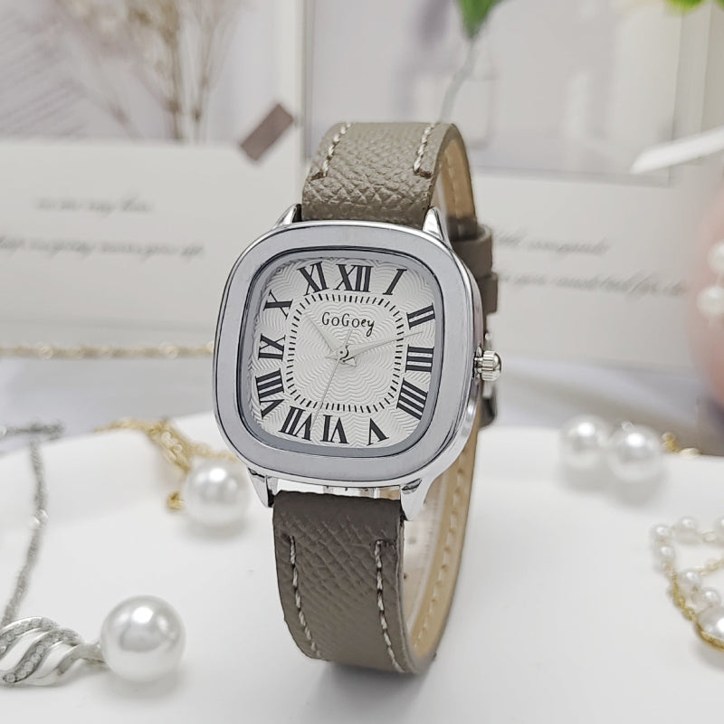 Watch with a gray strap and silver case on a white surface with pearls