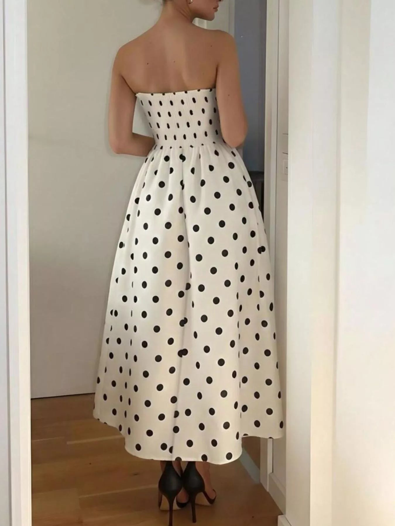 Woman wearing a white strapless dress with black polka dots, standing in a room.