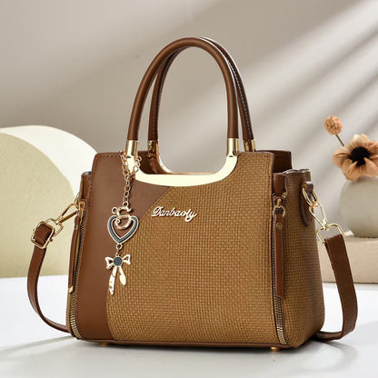 Small square crossbody bag, dark brown textured fabric, zipper, top handles, heart and bow charm.