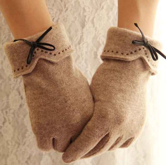 Pair of beige gloves with black ribbons on a textured white background