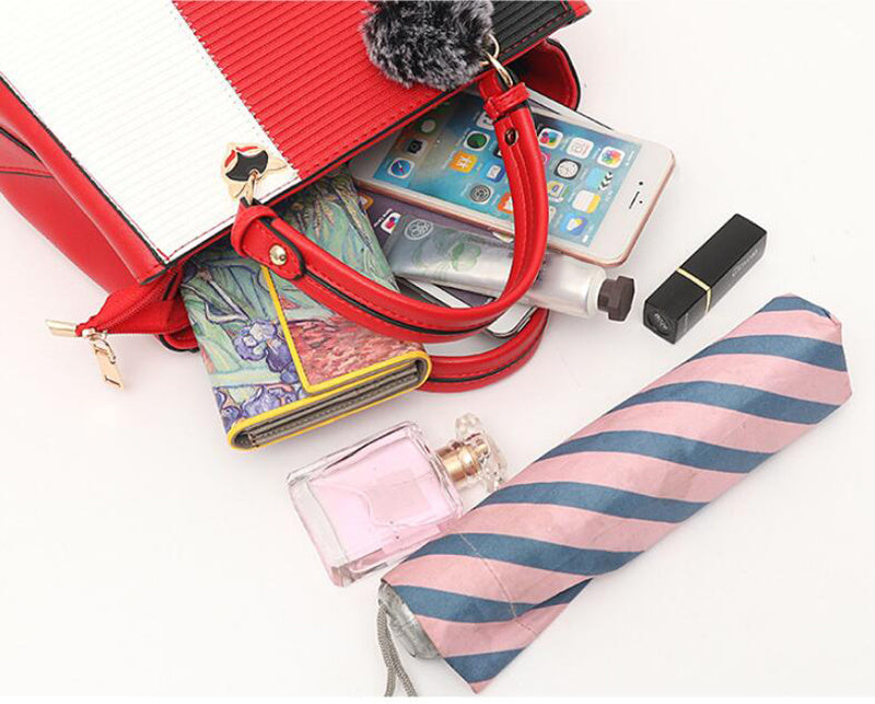 Open red handbag with phone, wallet, lipstick, and striped umbrella on a white background
