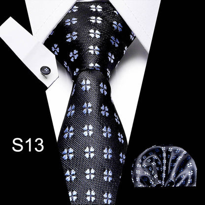 Black tie with white floral pattern, pocket square, and cufflink set on a white background