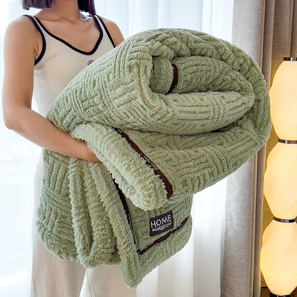 Person holding a green textured blanket with 'HOME' branding in a softly lit room.