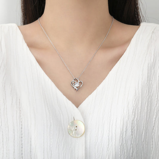 Silver necklace with a heart-shaped pendant worn by a person in a white shirt.