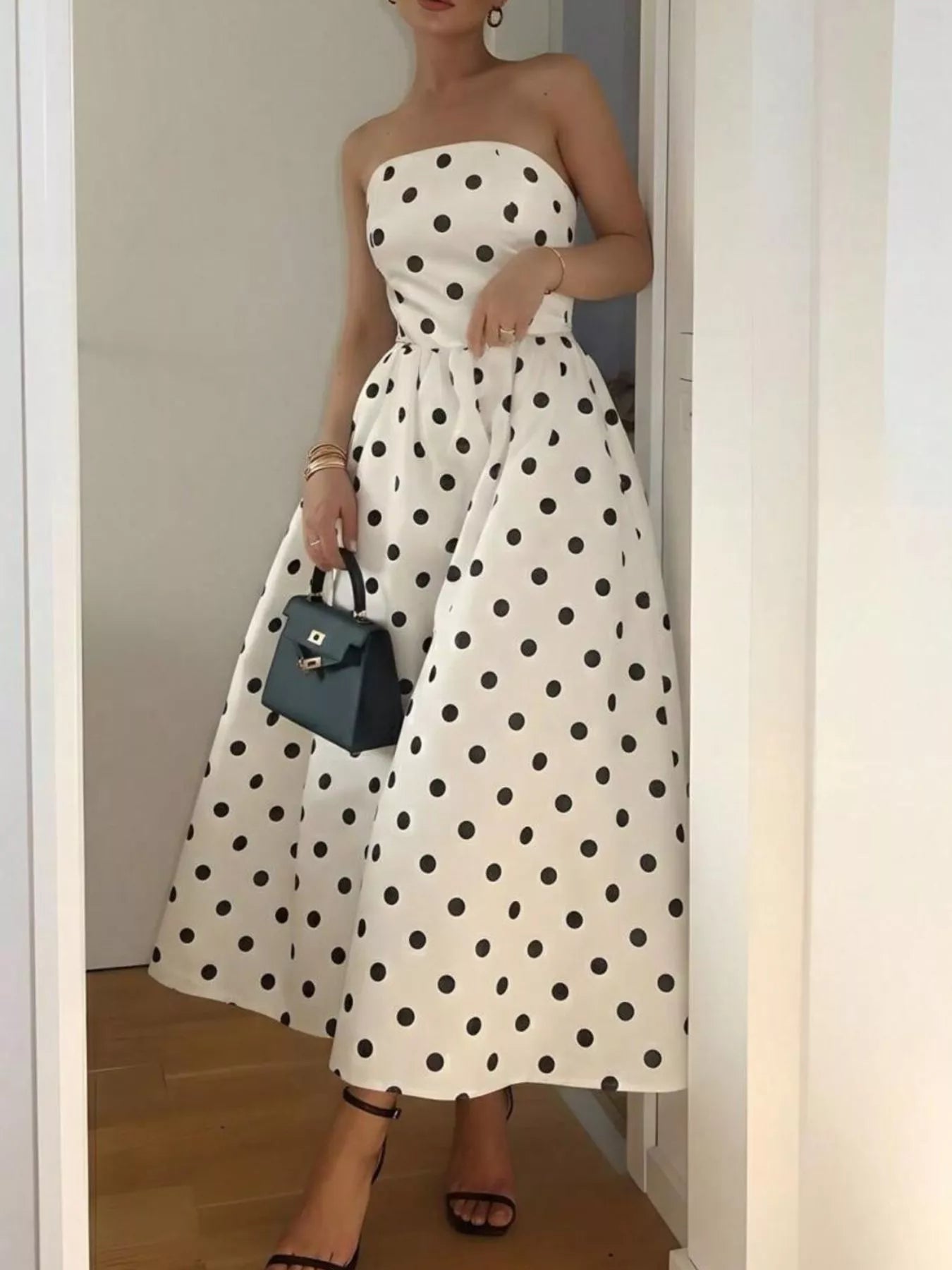 Woman wearing a white strapless dress with black polka dots, holding a black handbag.