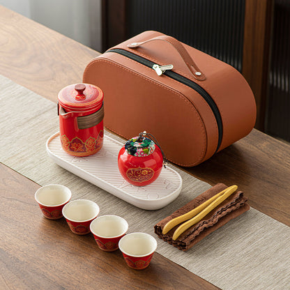 Tea set with red teapot, cups, and decorative item on a wooden table.