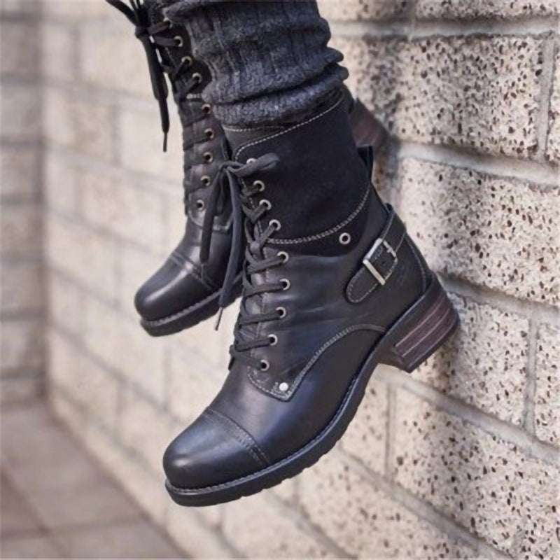 Black leather boots with buckles worn by a person against a brick wall.