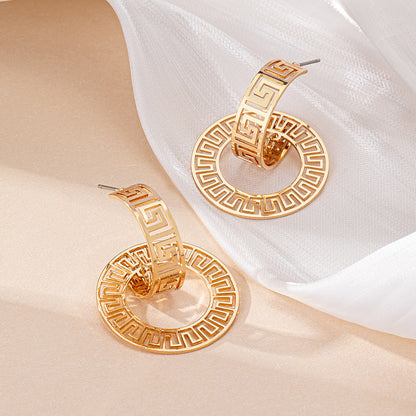 Gold hoop earrings with intricate design on a beige and white fabric background
