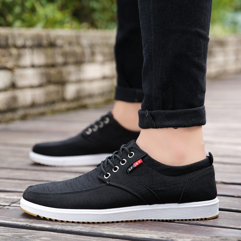 Black casual shoes worn with black pants on a wooden floor.