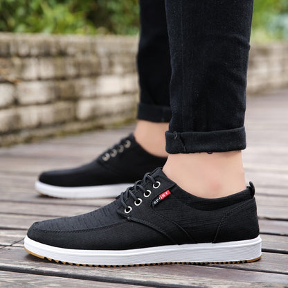 Black casual shoes worn with black pants on a wooden floor.