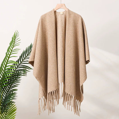 Beige fringe poncho on a hanger with a plant in the corner