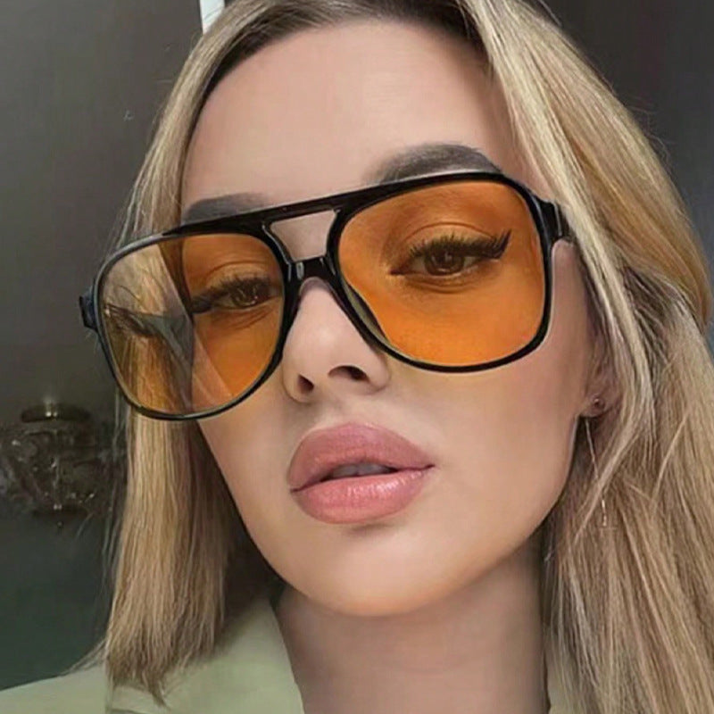 Close-up of a person wearing large sunglasses with orange lenses.