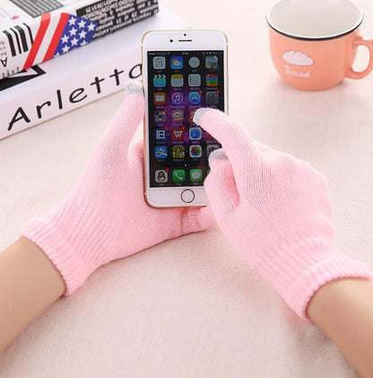 Person using a smartphone with pink gloves on a desk with a mug and books.