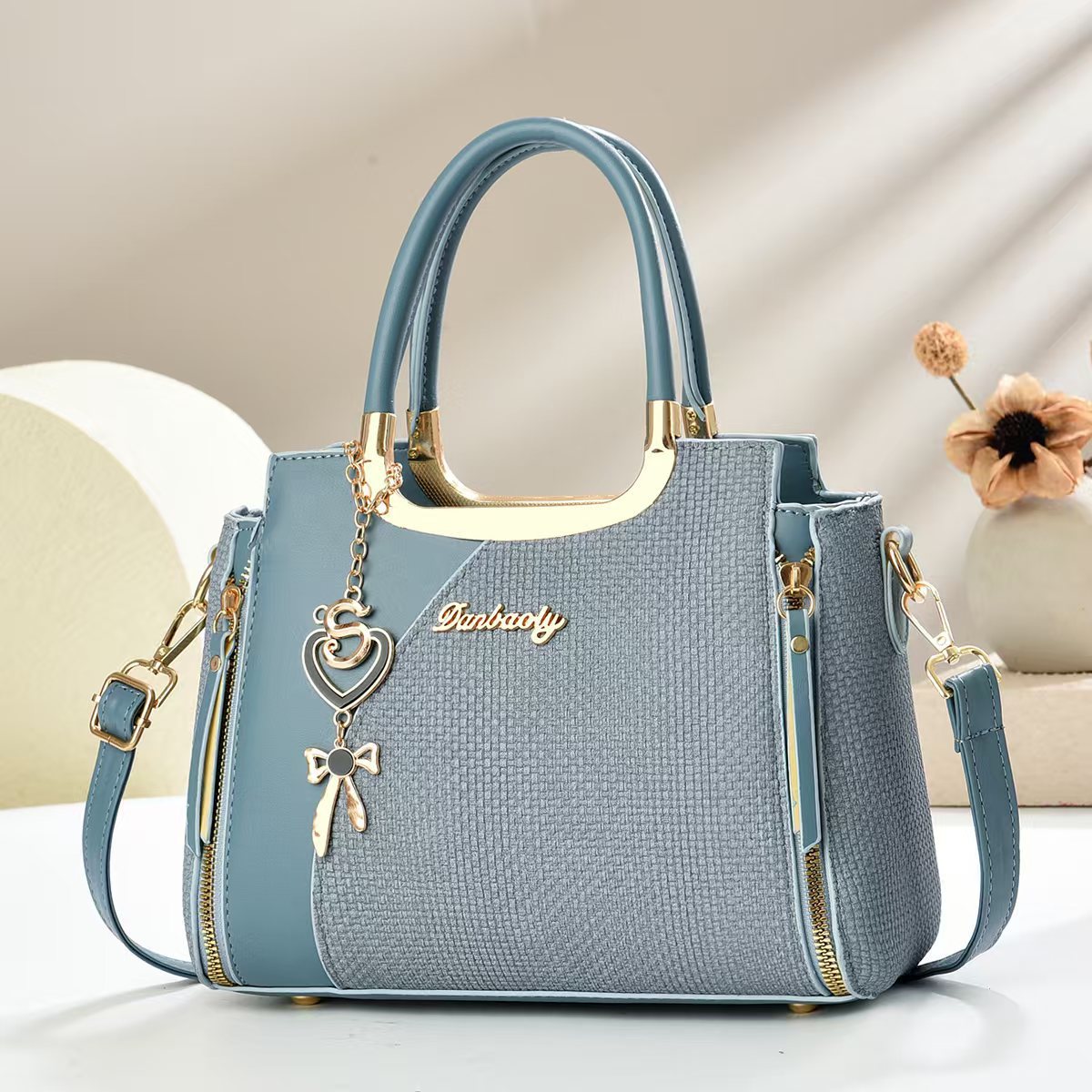 Light blue small square crossbody bag with top handles and gold zipper, heart and bow charm