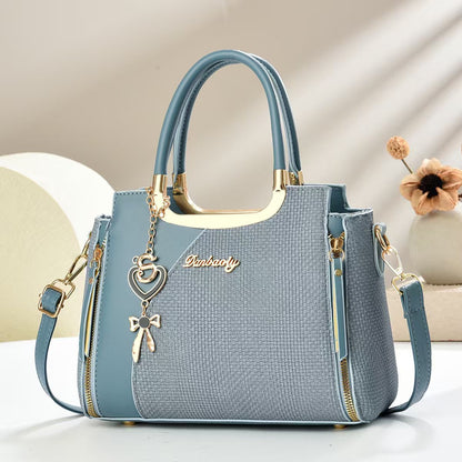 Light blue small square crossbody bag with top handles and gold zipper, heart and bow charm