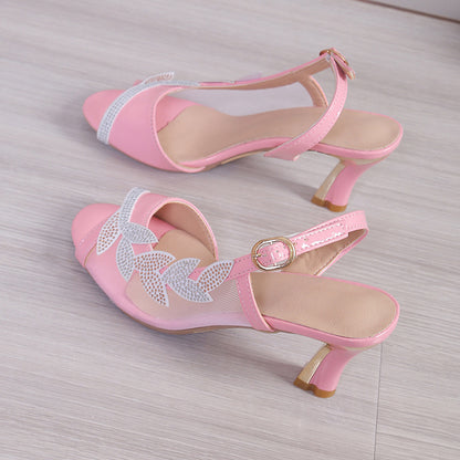 Pair of pink high-heeled shoes with decorative elements on a light wooden floor.
